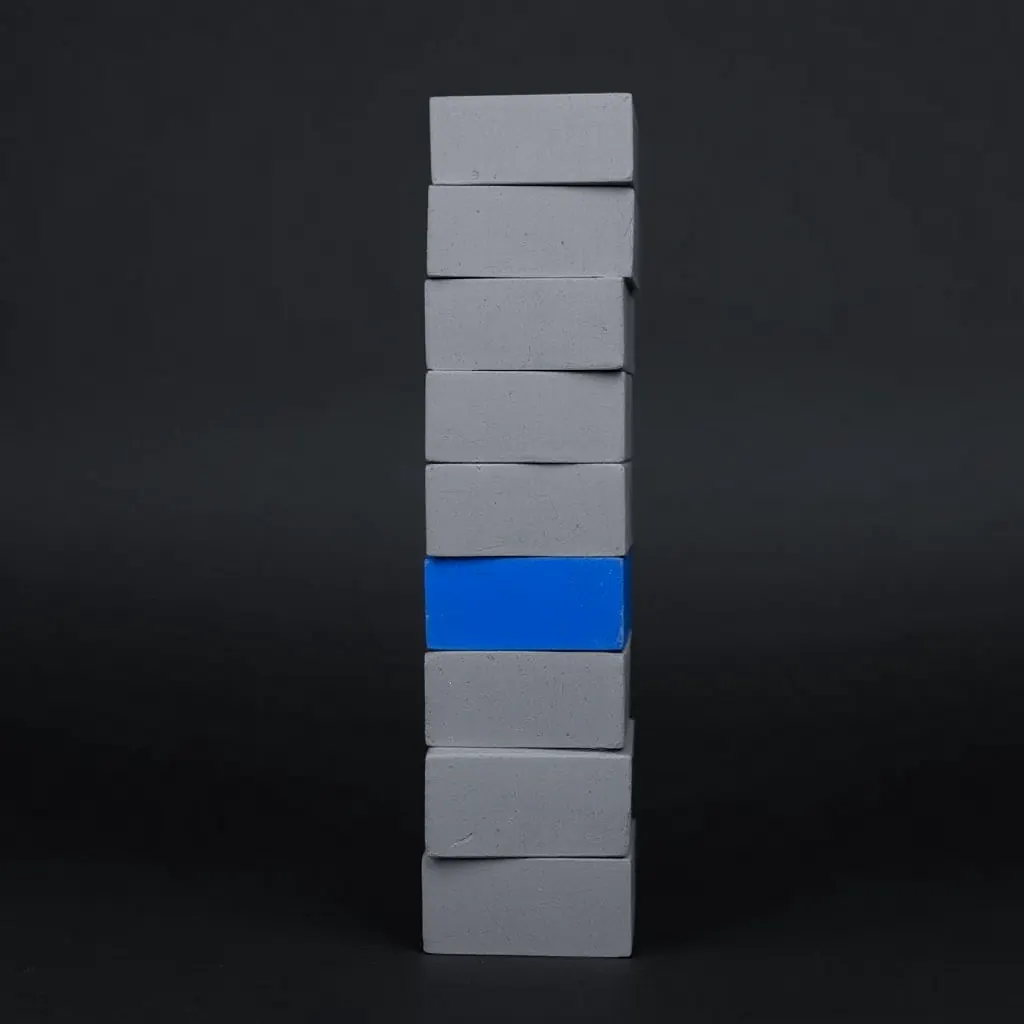 A tower of stone blocks standing straight and even, one block in its middle blue.